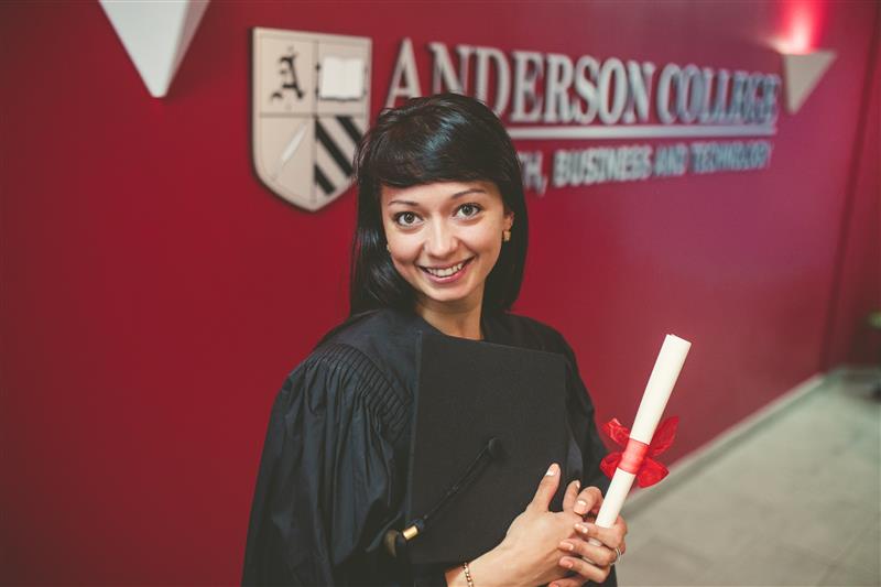 An Anderson College graduate in cap and gown holding her diploma